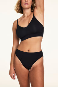 On a light studio backdrop, Sonnie wears the Cloud Cotton French Cut in Black with a matching black bra. The underwear features a high-rise fit and high-cut leg openings. sizing: Sonnie wears size Large