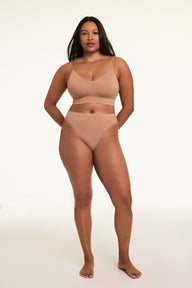 In a softly lit studio, Alana wears the Cloud Cotton Thin Strap Bralette and Cloud Cotton French Cut Brief in Dune. The bralette features thin adjustable straps and soft cotton modal fabric, paired with a high-rise French cut brief with a high leg silhouette and moderate coverage.
