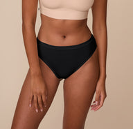 Front view of Victoria wearing the Cloud Cotton Highwaist Thong in Black. The image focuses on the soft, high-rise waistband and full front coverage made from breathable cotton fabric. sizing: Victoria wears size Medium