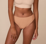 Victoria wearing the Cloud Cotton Highwaist Thong in Dune. The image showcases the thong’s wide waistband and high-leg cut, offering light compression and a smooth, barely-there feel thanks to its super-soft cotton-modal blend. sizing: Victoria wears size Medium