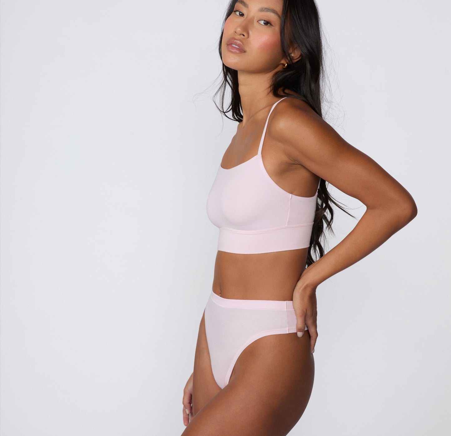 On a clean studio backdrop, a side view shows a model wearing the Cloud Cotton Highwaist Thong in Primrose with the matching Cloud Cotton Thin Strap Bralette, highlighting the high-rise waistband and smooth cotton modal fabric.