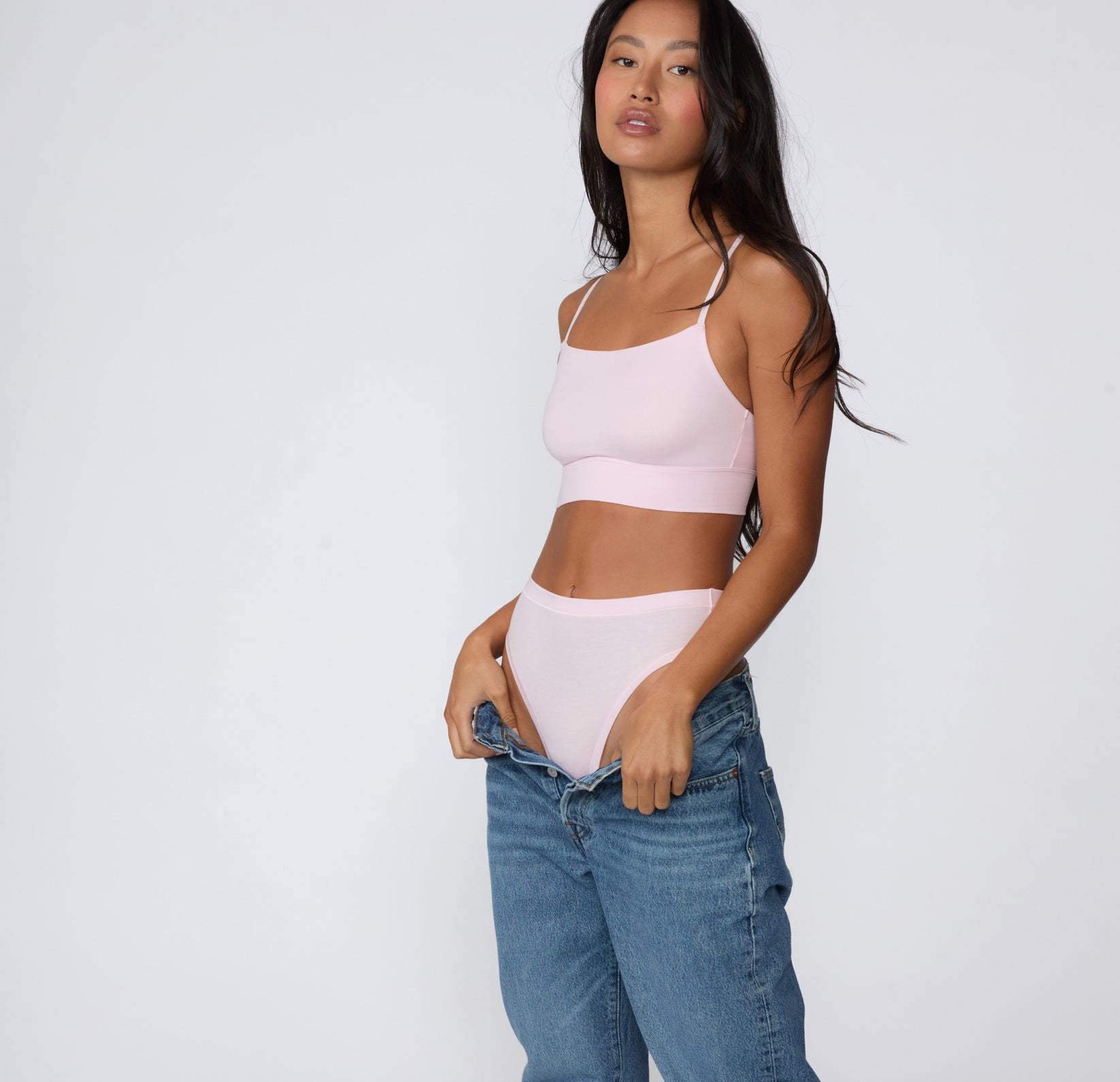 On a clean studio backdrop, a full-body view shows a model wearing the Cloud Cotton Highwaist Thong in Primrose with the matching Cloud Cotton Thin Strap Bralette, styled with denim and highlighting the smooth high-rise fit.