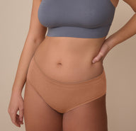 Sonnie wears the Cloud Cotton Hiphugger in Dune, shown from the front with one hand on her hip. The mid-rise cut and soft, stretch cotton modal fabric offer full front coverage and a smooth fit. sizing: Sonnie wears size Large