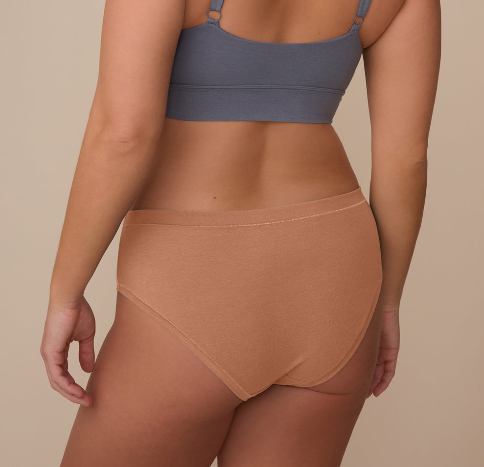 Back view of model Sonnie wearing the Cloud Cotton Hiphugger in Dune. The image highlights the full back coverage and comfortable waistband that stays in place without digging.