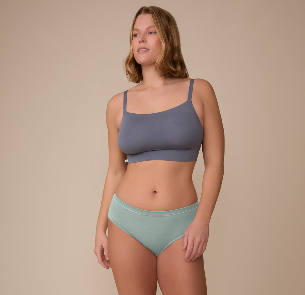Model Sonnie stands in a relaxed pose wearing the Cloud Cotton Hiphugger in Seaglass and the Cloud Cotton Thin Strap Bralette. The image shows the underwear’s natural fit and breathable cotton modal blend.