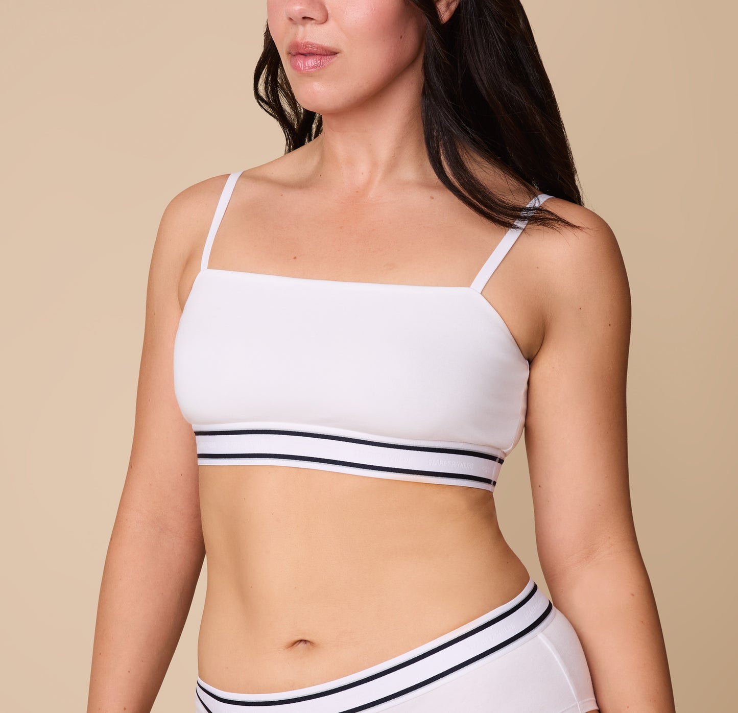 A close-up of Emersyn wearing the Cloud Cotton Retro Bandeau Bralette in White. The straight neckline and thin adjustable straps offer a sleek and minimal look, while the striped elastic underband adds a sporty touch. sizing: Emersyn wears size Large