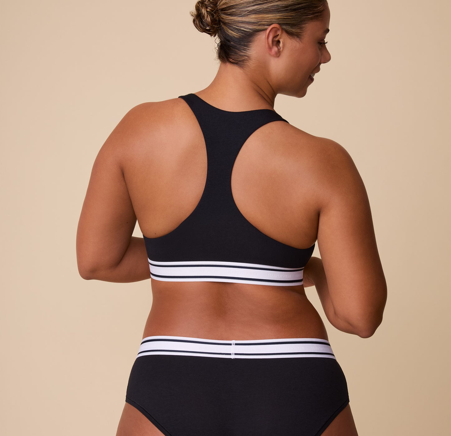India showcases the full racerback cut of the Cloud Cotton Retro Racerback Bralette from behind, emphasizing the supportive and flattering fit.
