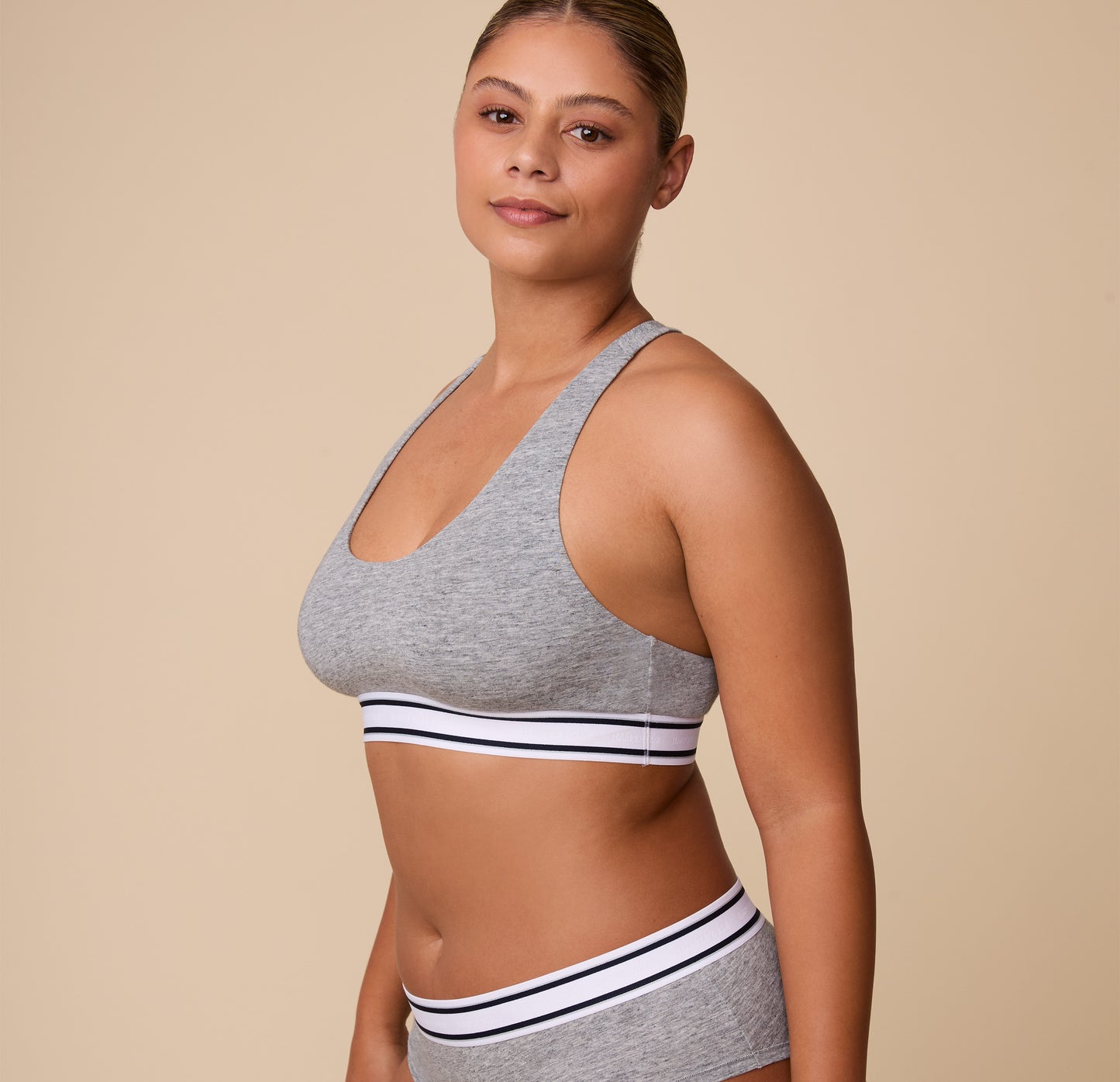 A relaxed three quarter profile of India in the Cloud Cotton Retro Racerback Bralette in Heather Charcoal, showcasing the smooth cotton fabric and contoured fit.