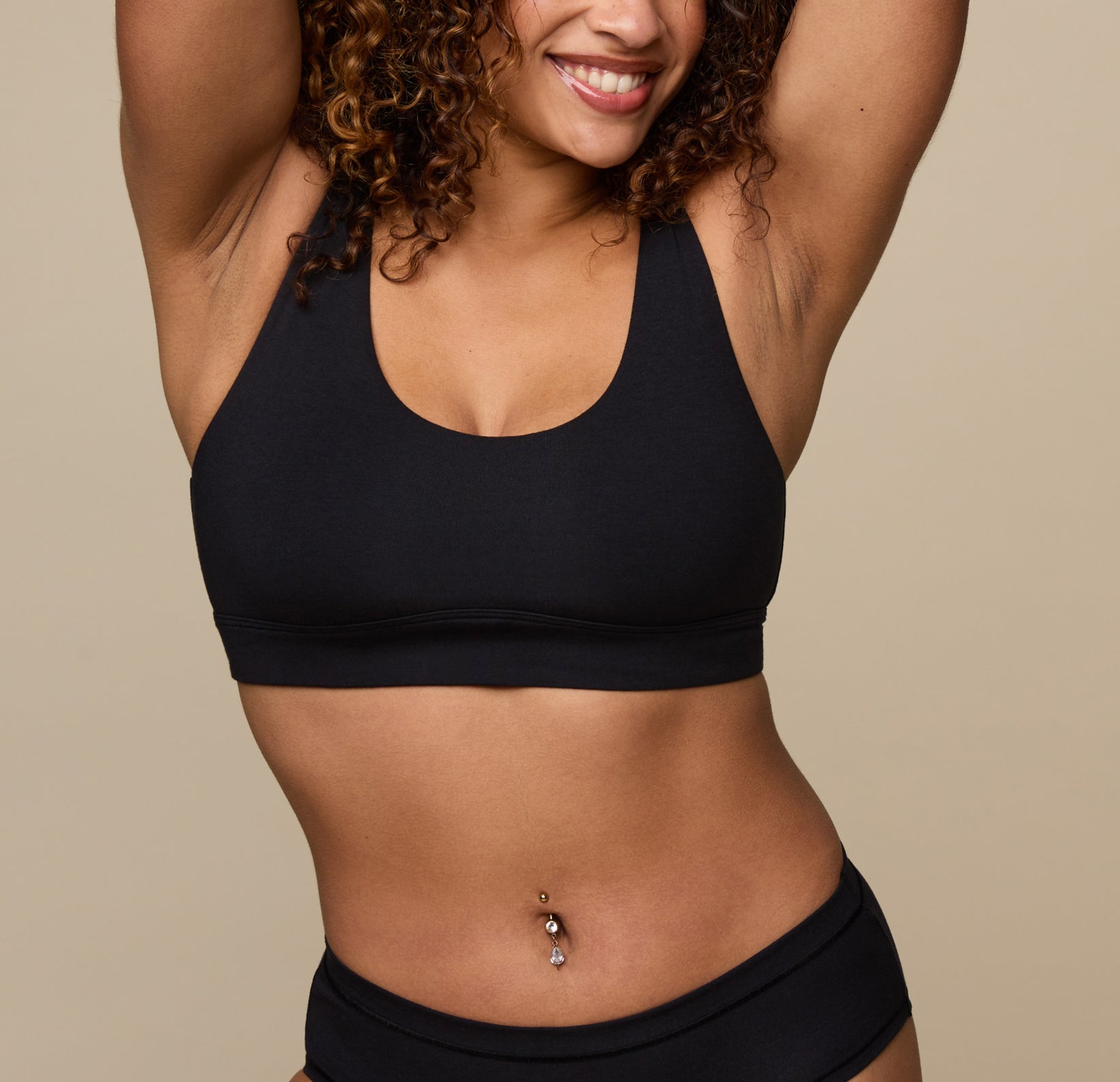 Jade lifts her arms and smiles, wearing the Cloud Cotton Scoop Bralette in Black. The front view shows the wide straps and soft scoop neckline, emphasizing the breathable cotton-modal blend and light support. sizing: Jade wears size Medium
