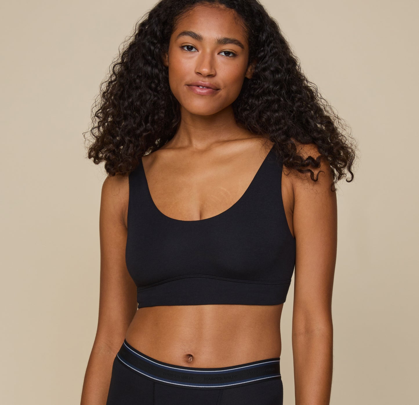 Zoe stands facing forward in the Cloud Cotton Scoop Bralette in Black. The bralette’s scoop neckline and supportive band are shown clearly, offering a casual, lounge-ready look. sizing: Zoe wears size Small