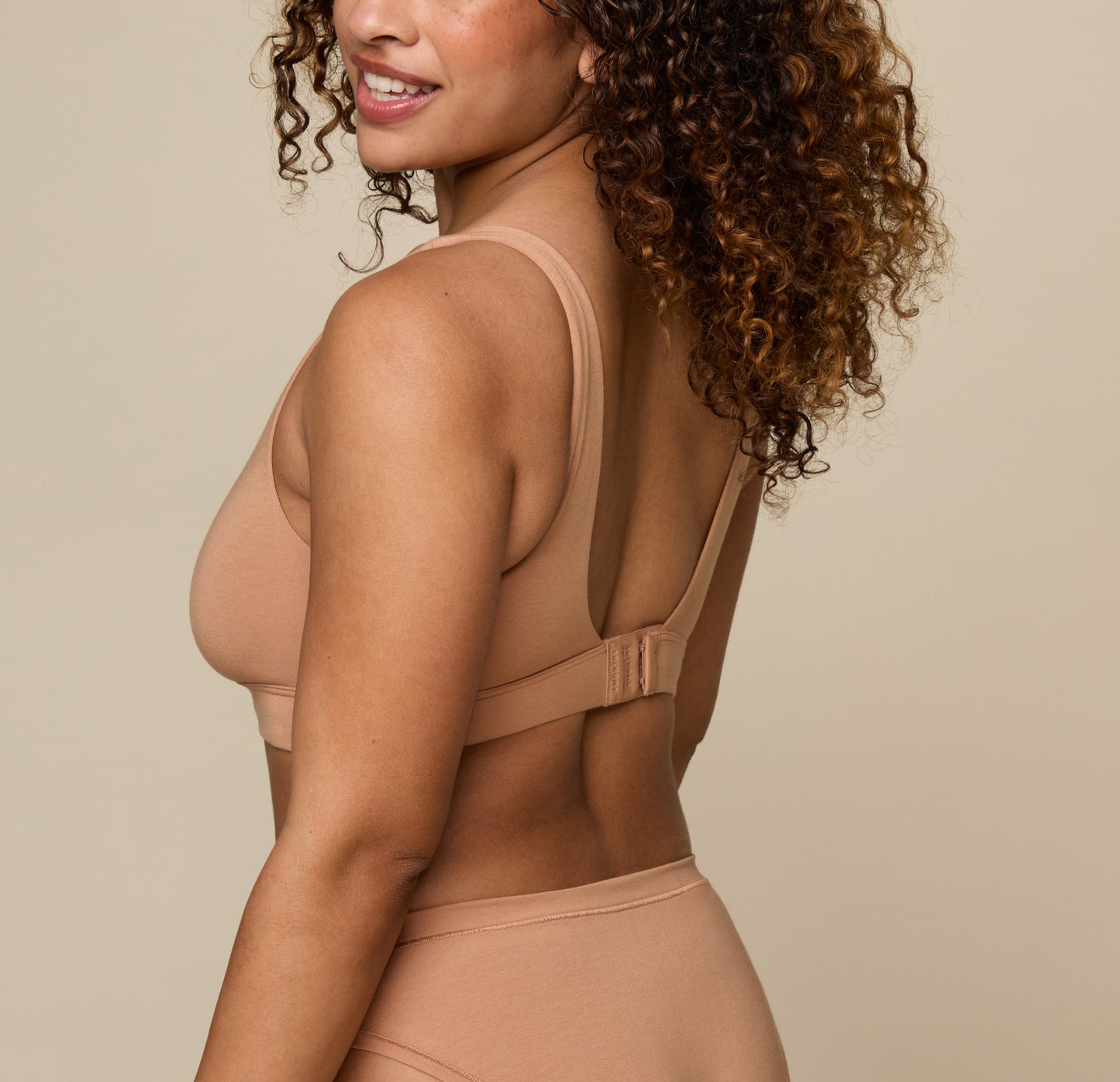 Back view of Jade wearing the Cloud Cotton Scoop in Dune. The low scoop back and hook and eye clasps are emphasized. 