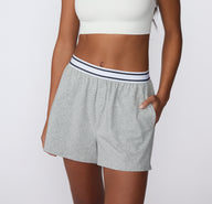 On a white studio backdrop, a close-up of the CloudCotton Short in Heather Grey focuses on the elastic waistband with subtle stripe detailing and soft gathered fabric below.