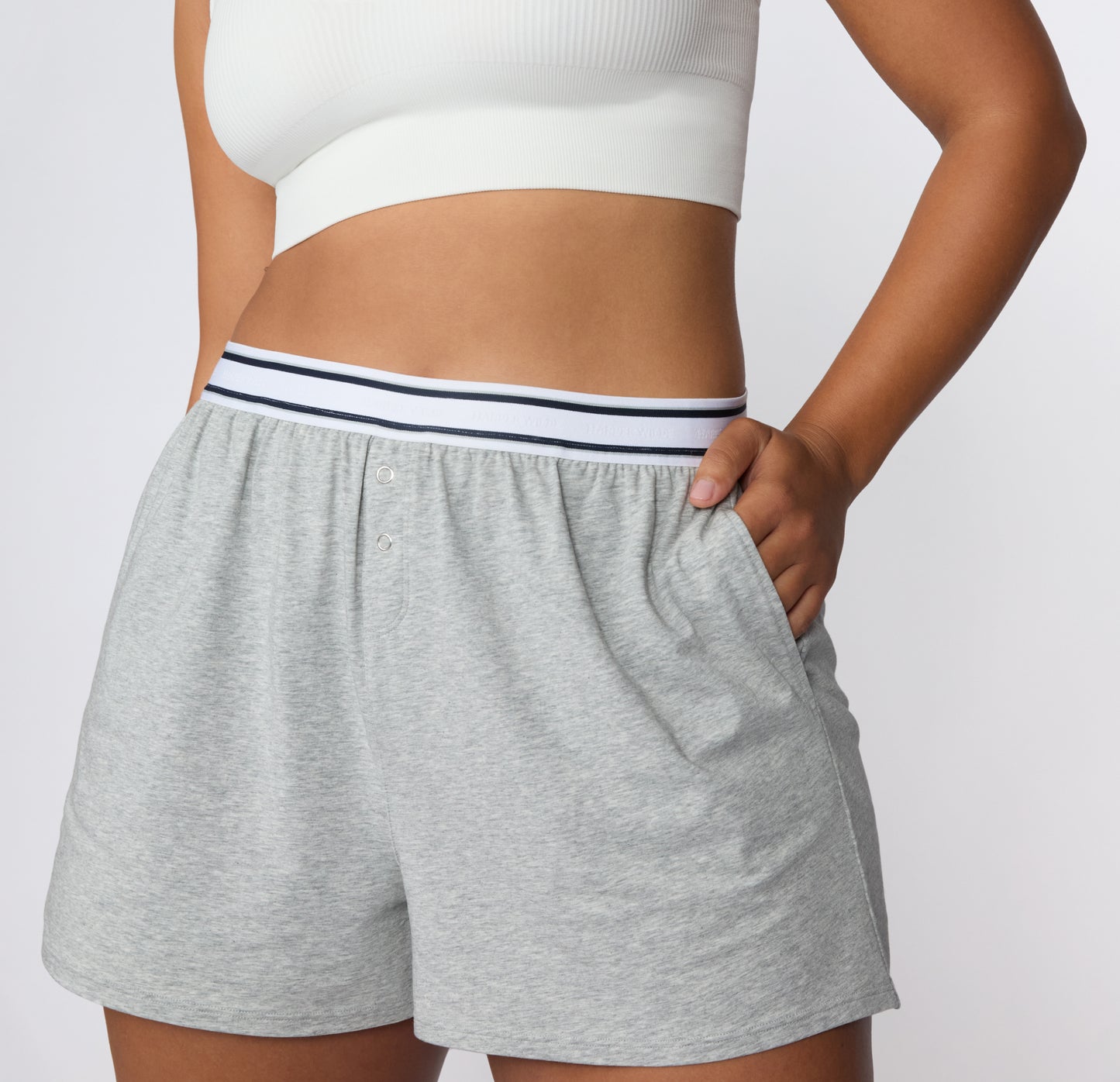 On a white studio backdrop, a full-body view shows the CloudCotton Short in Heather Grey paired with a white bralette, emphasizing the lightweight drape and comfortable lounge fit.