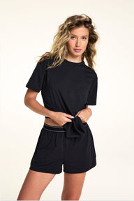 In a studio setting, Alexis wears the Cloud Cotton Shorts in Black with the matching Cloud Cotton Tee, featuring a relaxed fit, soft fabric, elastic waistband with contrast stripe detailing, and front button detail.