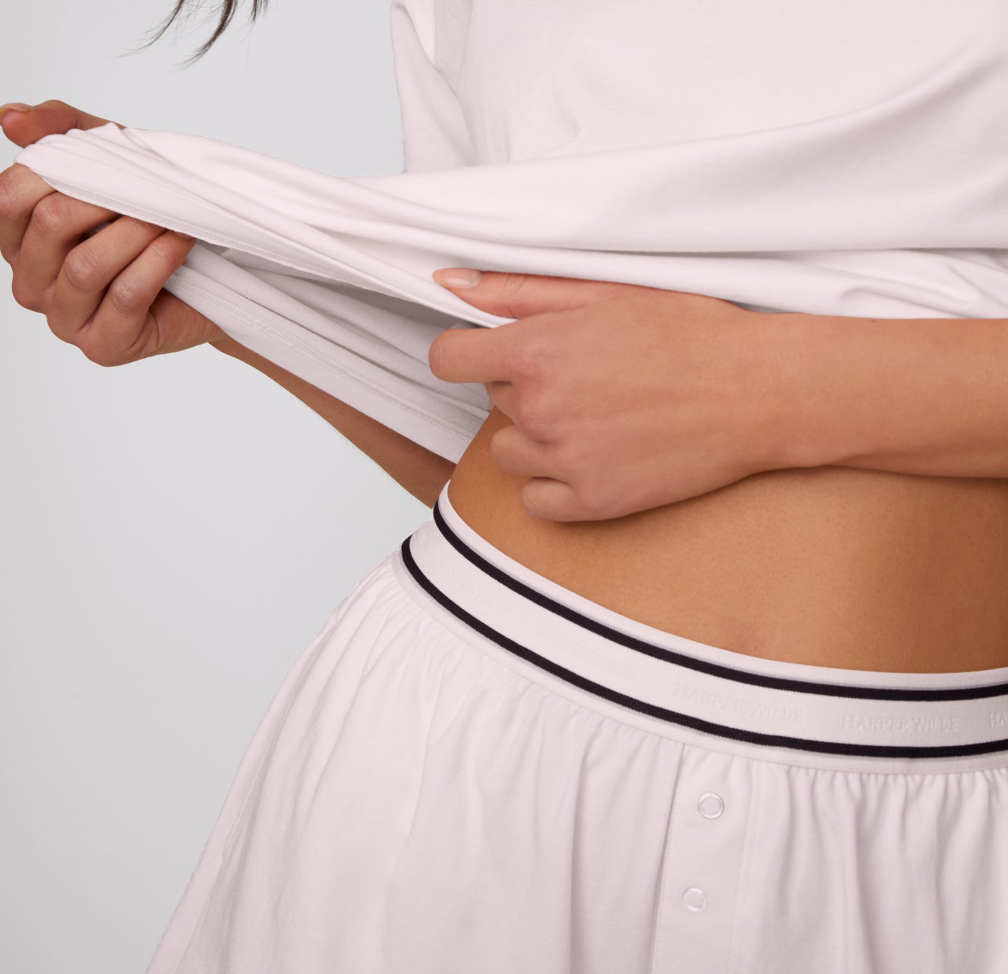 On a clean studio backdrop, a close-up shows hands stretching the Cloud Cotton Tee above the Cloud Cotton Short in Primrose, highlighting the smooth, flexible cotton modal fabric and elastic waistband.