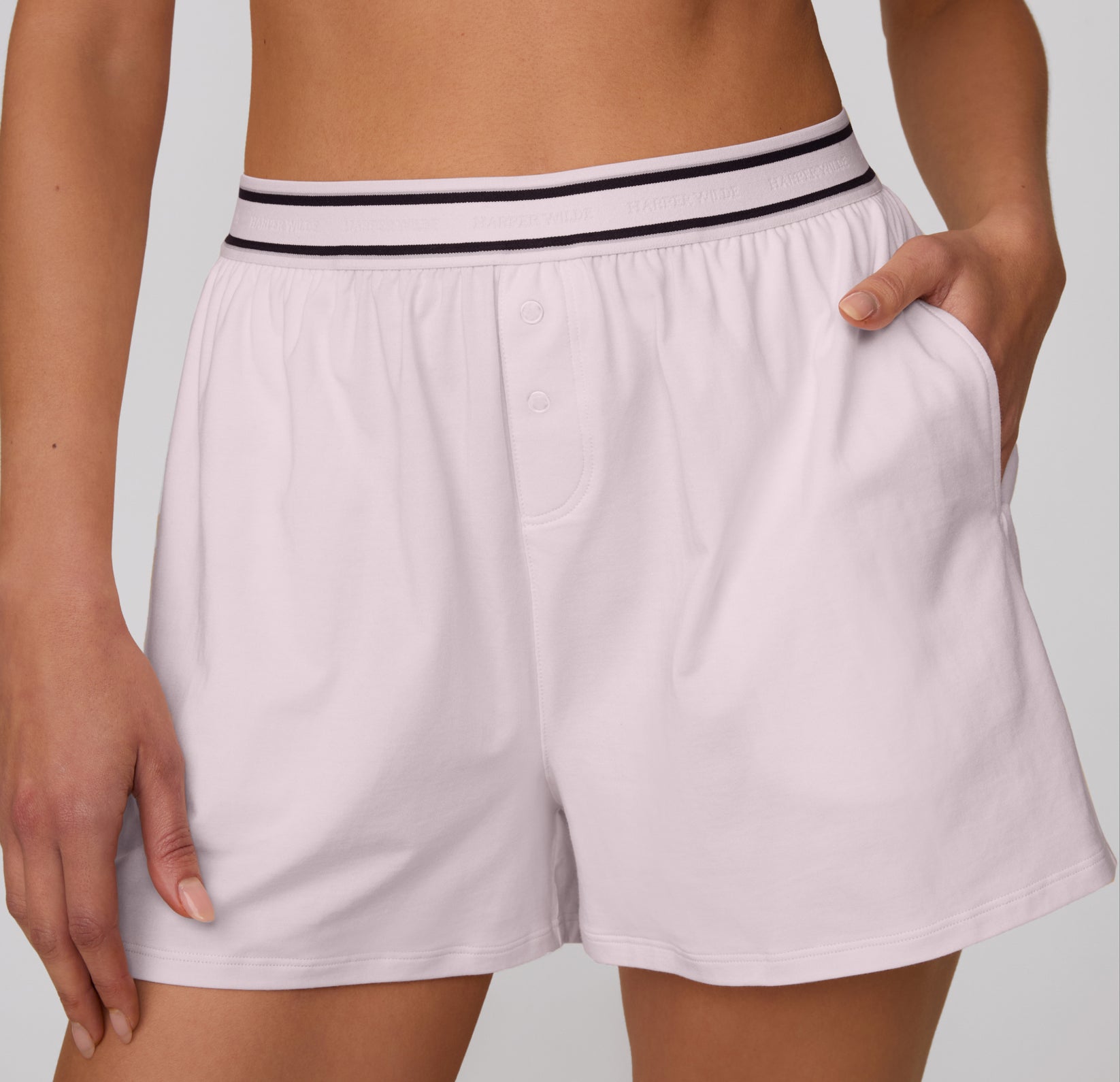 On a clean studio backdrop, a front close-up shows the Cloud Cotton Short in Primrose, featuring the elastic waistband, button-front detail, and soft cotton modal fabric.
