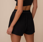 Back view of Marcela wearing the Cloud Cotton Sleep Short in Black. The image highlights the relaxed leg opening and gathered waistband that sits comfortably on the hips.