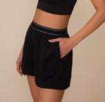 Side view of Marcela with one hand in the pocket of the Cloud Cotton Sleep Short in Black. The image shows the soft drape of the modal-cotton fabric and the stretchy waistband.