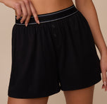 Zoomed-in front view of Marcela wearing the Cloud Cotton Sleep Short in Black. Focus on the double snap fly detail and soft-touch waistband.