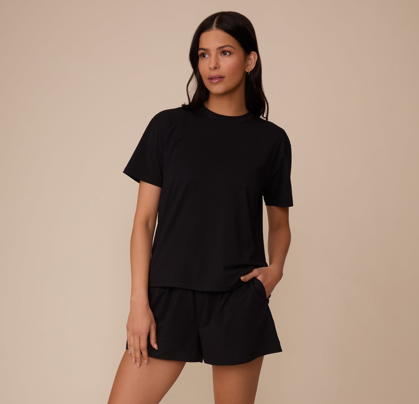 Full body shot of Marcela wearing the Cloud Cotton Sleep Short and matching T-Shirt in Black. She stands with one hand in her pocket, showing the relaxed fit of the full sleepwear set.