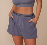 Close-up of Sonnie wearing the Cloud Cotton Sleep Short in Slate, paired with a matching Slate bralette. Her hands are in the pockets, highlighting the soft, relaxed fit and double snap fly design. sizing: Sonnie wears size Large