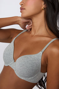 On a white studio backdrop, Amber wears the Cloud Cotton T-Shirt Bra in Heather Grey in a close-up side view, highlighting the lightly lined cups, soft cotton modal fabric, and slim adjustable straps.