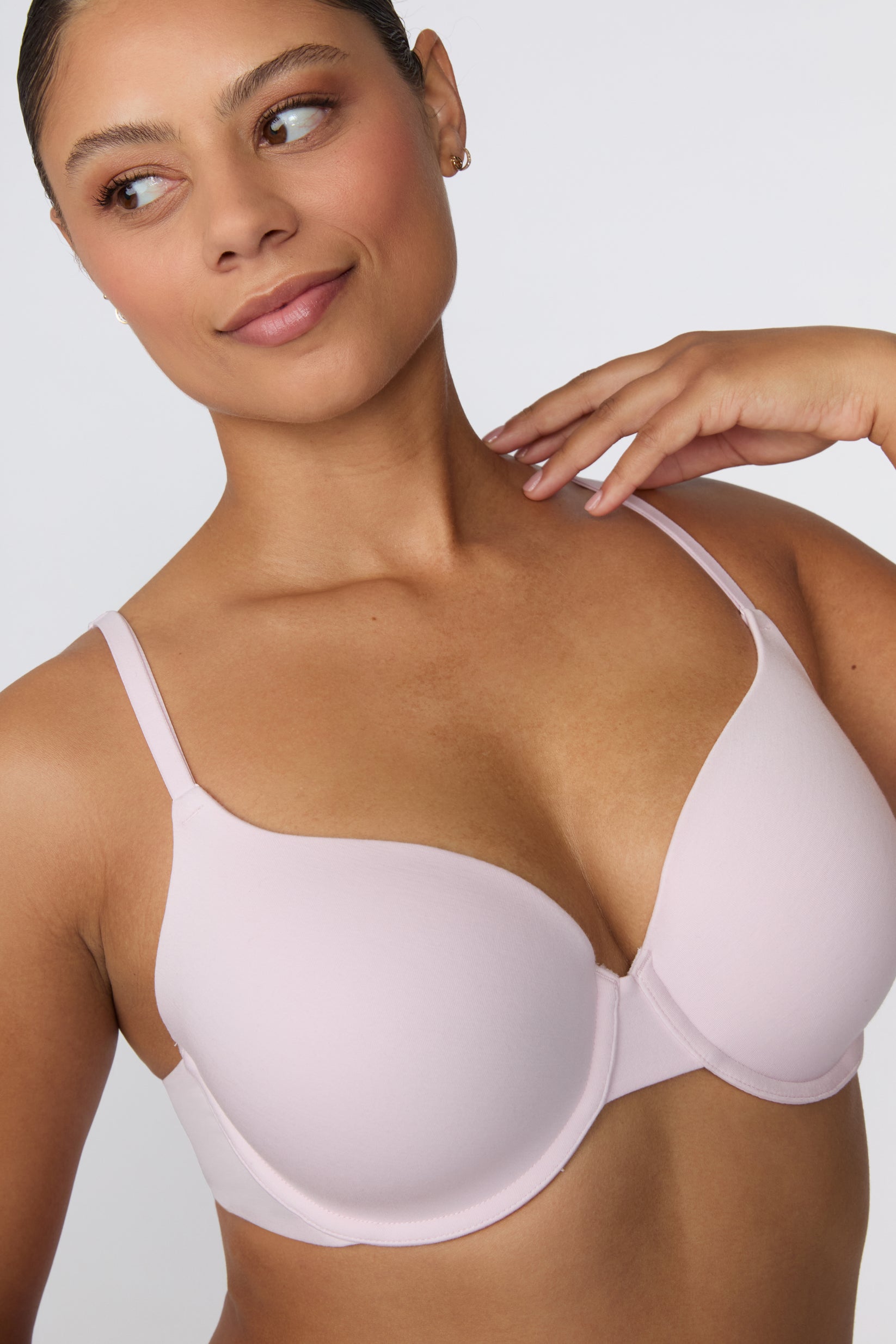 On a white studio backdrop, India wears the Cloud Cotton T-Shirt Bra in Primrose in a close-up three-quarter view, highlighting the lightly lined molded cups, smooth cotton modal fabric, and slim adjustable straps.