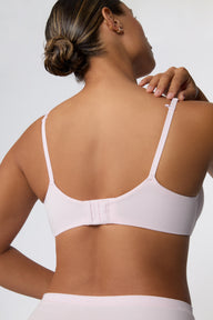 On a white studio backdrop, India wears the Cloud Cotton T-Shirt Bra in Primrose in a back three-quarter view, showing the adjustable straps, smooth cotton modal band, and low-profile back design.