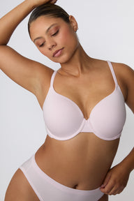 On a white studio backdrop, India wears the Cloud Cotton T-Shirt Bra in Primrose in a close-up three-quarter front view, highlighting the lightly lined cups, clean neckline, and soft cotton modal fabric.