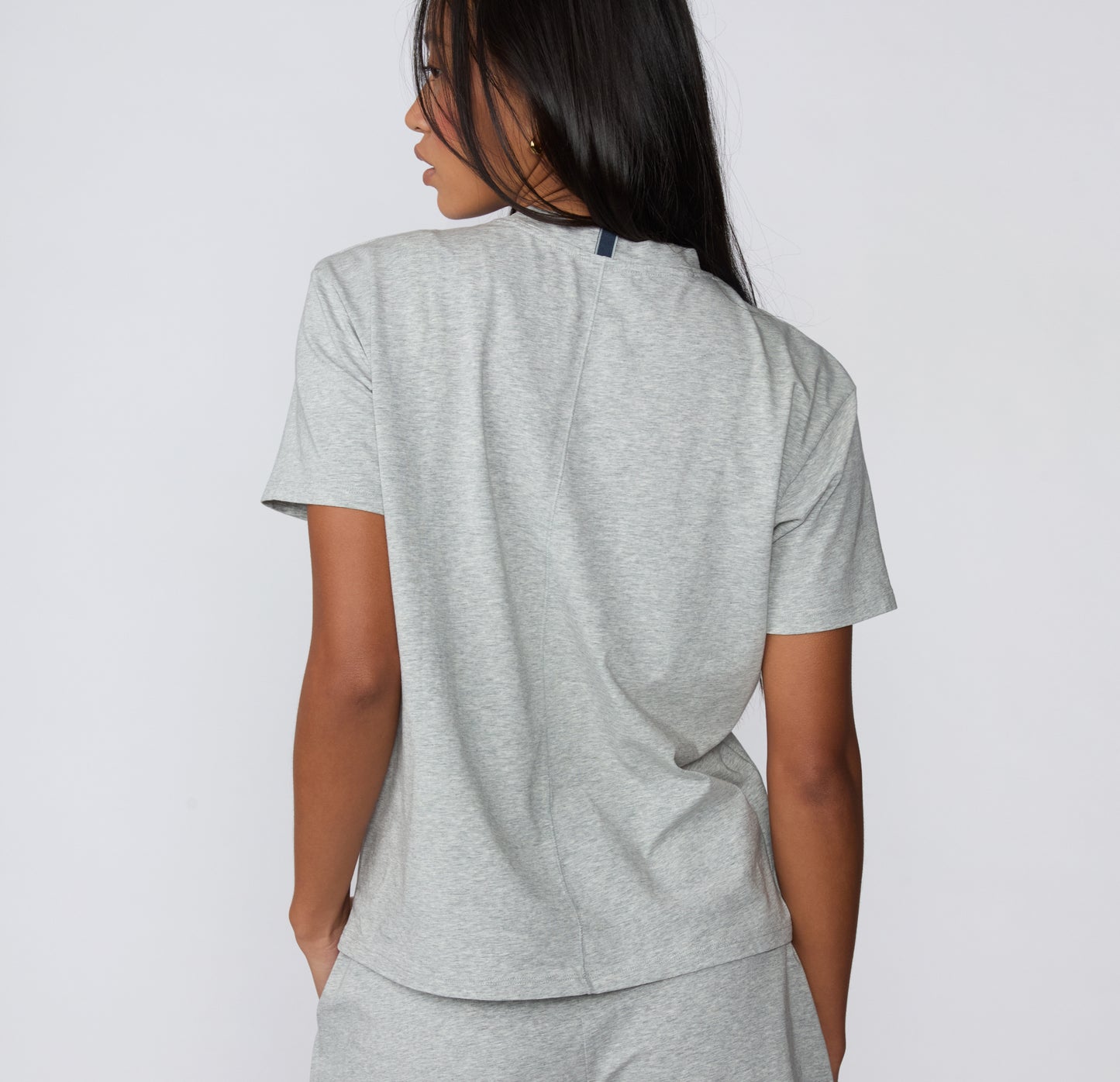 On a white studio backdrop, the Cloud Cotton Tee in Heather Grey is shown from the back, highlighting the relaxed silhouette and smooth cotton construction.