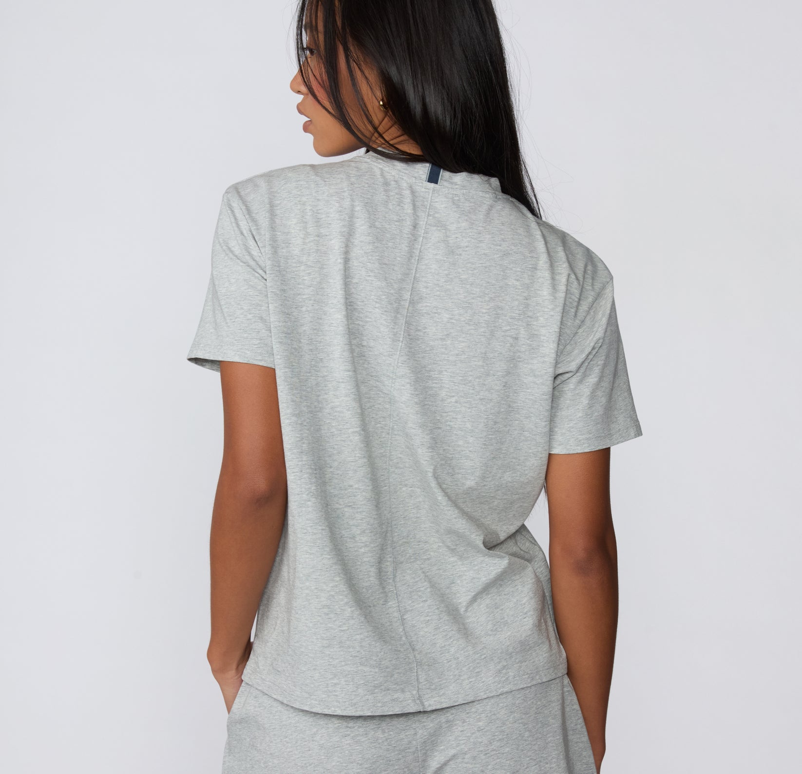 On a white studio backdrop, the Cloud Cotton Tee in Heather Grey is shown from the back, highlighting the relaxed silhouette and smooth cotton construction.