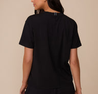 Back view of Marcela wearing the Cloud Cotton T-Shirt in Black. The shirt features a center seam detail and a relaxed fit through the shoulders and torso.