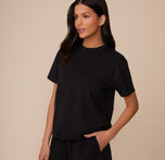 Three-quarter front view of Marcela in the Cloud Cotton T-Shirt in Black. She stands with one hand in her pocket, showing off the relaxed, everyday fit and classic crew neckline of the tee.