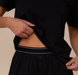 Zoomed-in detail of Marcela lifting the bottom of the Cloud Cotton T-Shirt in Black to show the branded waistband of the Cloud Cotton Short.