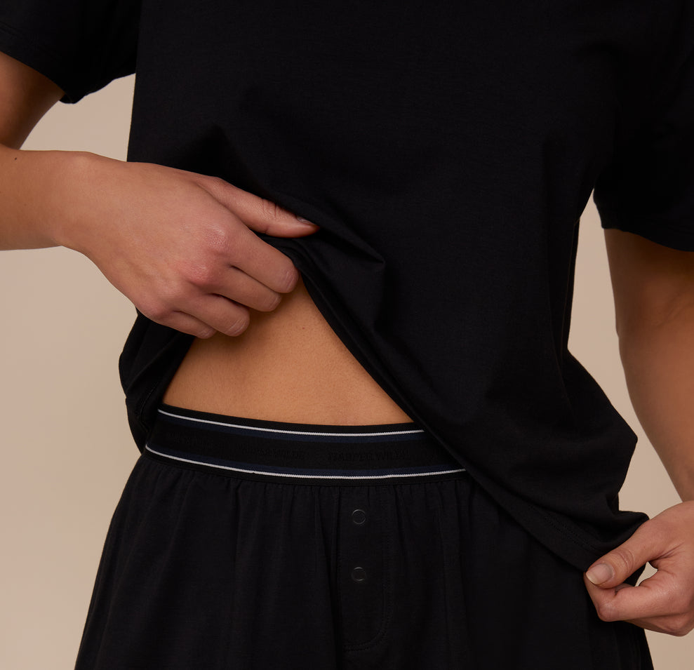 Zoomed-in detail of Marcela lifting the bottom of the Cloud Cotton T-Shirt in Black to show the branded waistband of the Cloud Cotton Short.
