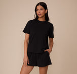Full body shot of Marcela wearing the Cloud Cotton T-Shirt and matching short in Black. She stands with one hand in her pocket, showcasing the full set’s casual, cozy fit.