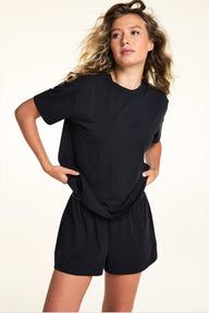 In a studio setting, Alexis wears the Cloud Cotton Tee in Black with matching Cloud Cotton Shorts, featuring a relaxed silhouette, crew neckline, and soft fabric designed for comfortable lounging.