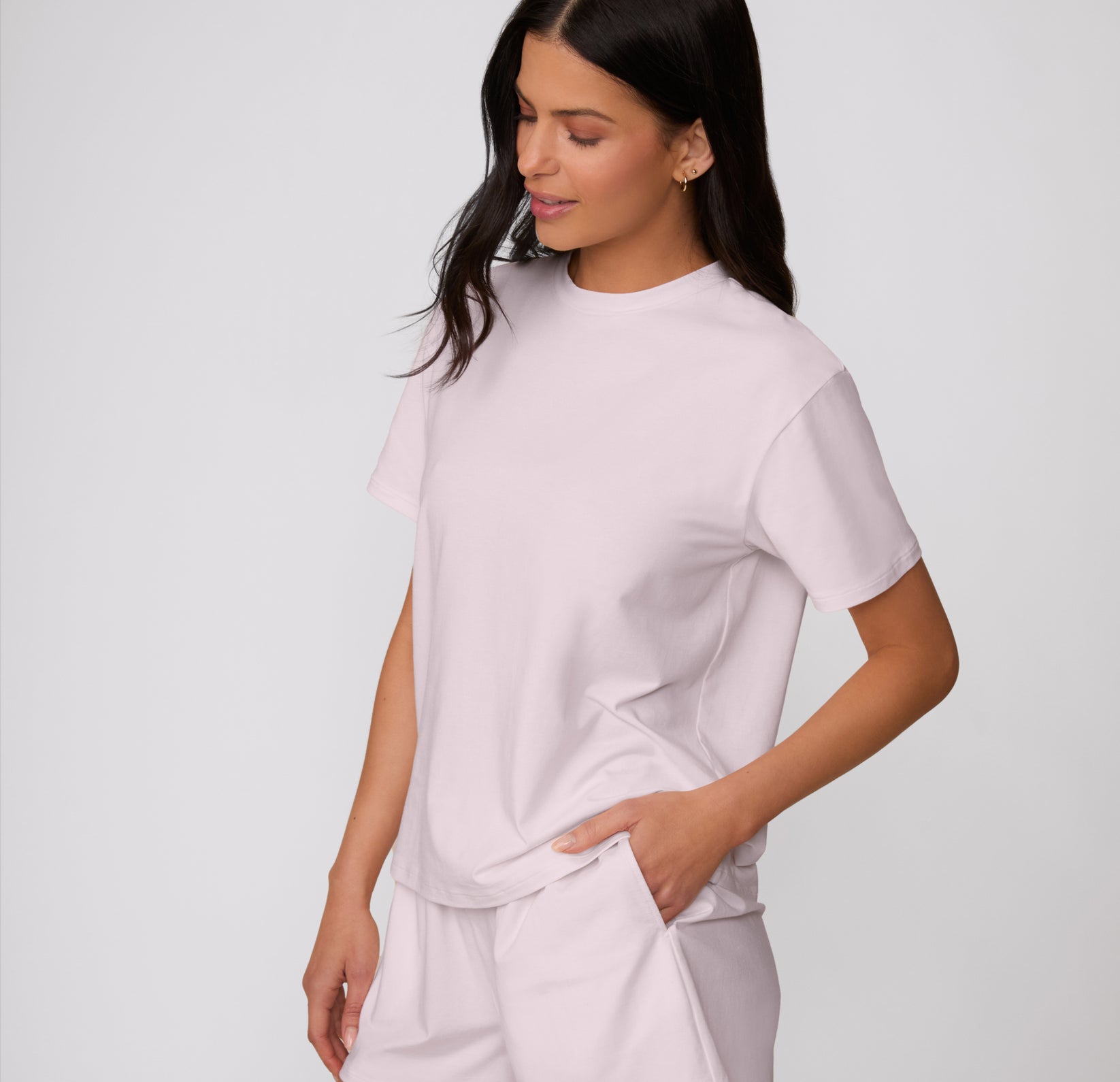 On a clean studio backdrop, a three-quarter front view shows a model wearing the Cloud Cotton Tee in Primrose, highlighting the relaxed silhouette and short sleeves.