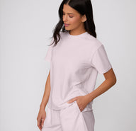 On a clean studio backdrop, a three-quarter front view shows a model wearing the Cloud Cotton Tee in Primrose, highlighting the relaxed silhouette and short sleeves.