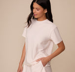 Three-quarter front view of Marcela in the Cloud Cotton T-Shirt in Quartz. She stands with one hand in her pocket, showing off the relaxed, everyday fit and classic crew neckline of the tee.