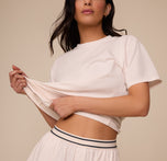 Zoomed-in detail of Marcela lifting the bottom of the Cloud Cotton T-Shirt in Quartz to show the branded waistband of the Cloud Cotton Short. 
