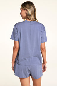 In a softly lit studio, Meagan wears the Cloud Cotton Tee and Cloud Cotton Short in Slate, shown from the back. The relaxed-fit tee features short sleeves and soft cotton modal fabric, paired with matching lounge shorts designed for easy everyday comfort.