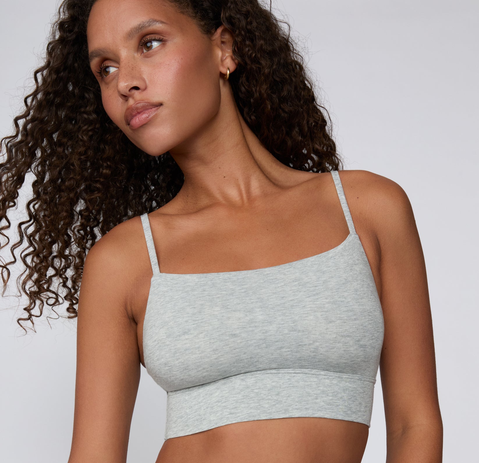 On a light studio backdrop, a model wears the Cloud Cotton Thin Strap Bralette in Light Heather Grey, shown from the front with a square neckline, thin adjustable straps, and a soft longline underband.