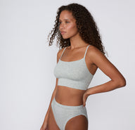 On a light studio backdrop, the Cloud Cotton Thin Strap Bralette in Light Heather Grey is shown in a side view, highlighting the smooth cotton modal fabric, thin straps, and supportive longline fit.