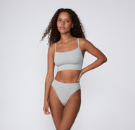 Full-body view on a light studio backdrop of the Cloud Cotton Thin Strap Bralette in Light Heather Grey, paired with matching underwear, showing the longline underband and thin adjustable straps.