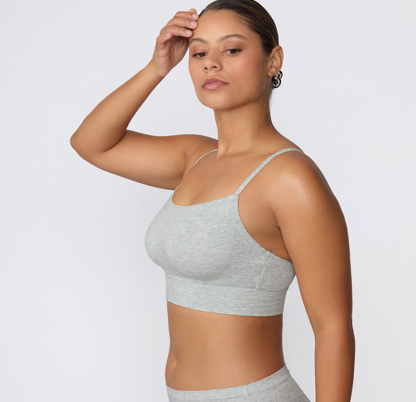 Side view on a light studio backdrop of the Cloud Cotton Thin Strap Bralette in Light Heather Grey, showing the slim straps, soft structure, and longline fit under the bust.