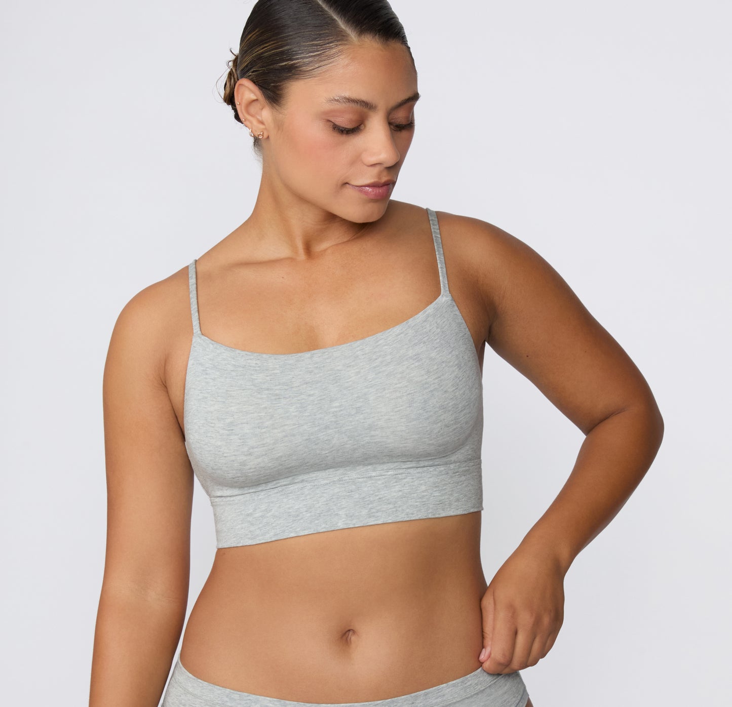 On a light studio backdrop, the Cloud Cotton Thin Strap Bralette in Light Heather Grey is shown from the front on a model looking downward, highlighting the square neckline, thin straps, and soft longline underband.