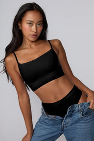 On a grey studio backdrop, Amber wears the Cloud Cotton Thin Strap Bralette in Black with matching black underwear and relaxed denim, featuring a straight neckline, thin adjustable straps, and soft cotton modal fabric. sizing: Amber wears size Small