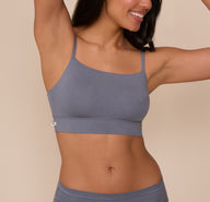  Close-up of Nemesis wearing the Cloud Cotton Thin Strap Bralette in Slate. The image highlights the slightly curved neckline, thin straps, and the smooth, stretchy fabric with minimal seams. sizing: Nemesis wears size Medium