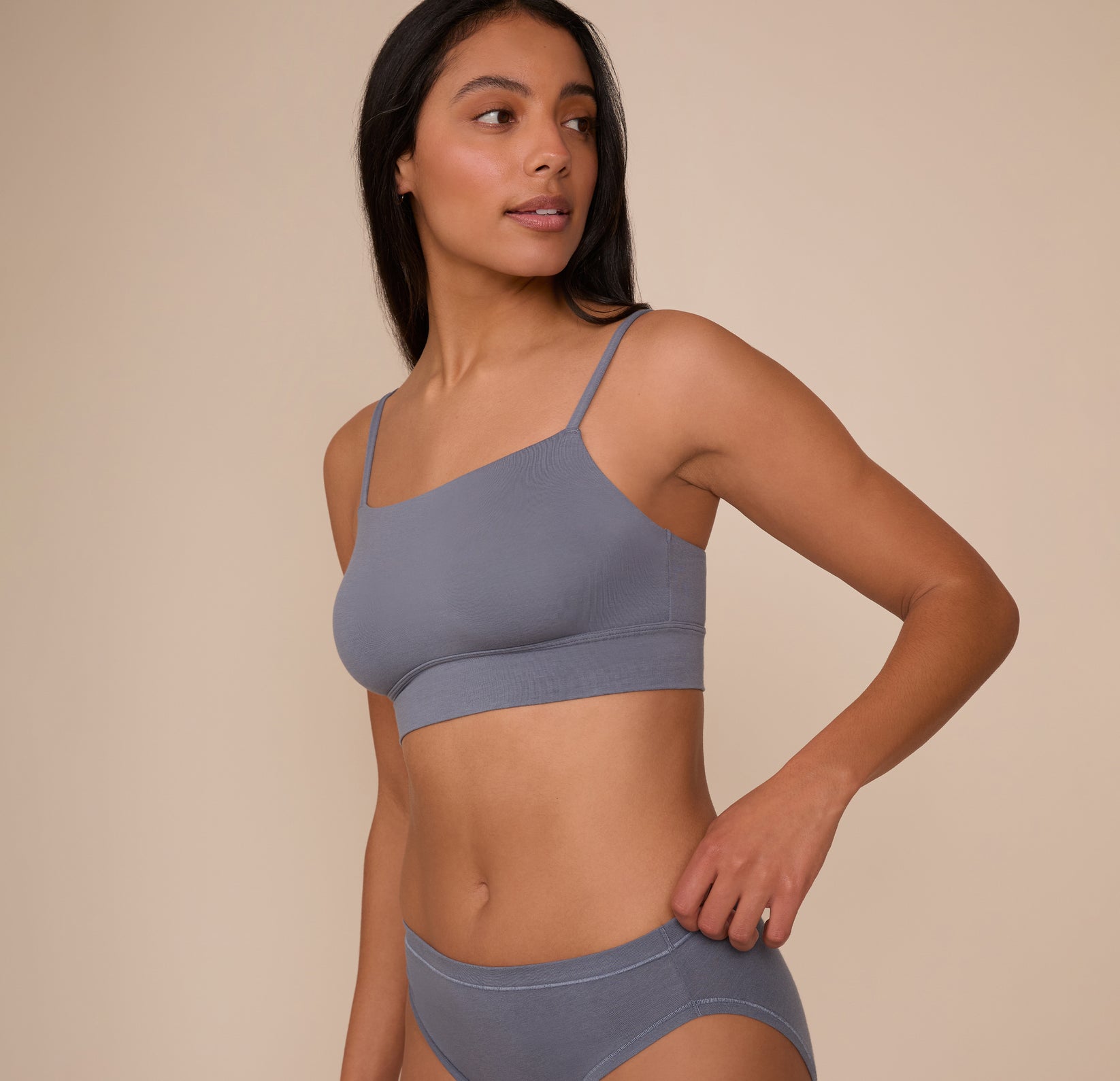 Side view of Nemesis wearing the Cloud Cotton Thin Strap Bralette and Cloud Cotton French Cut Brief in Slate. The angled shot shows the gentle curve of the neckline and the soft, body-hugging fit.